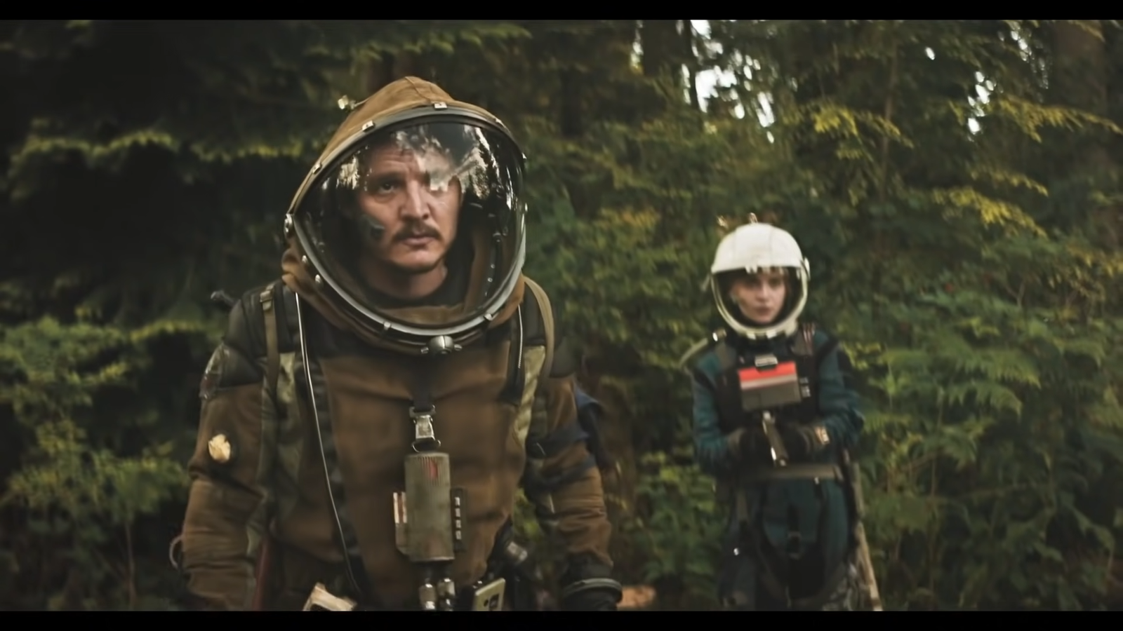two characters in protective suits near a tree line